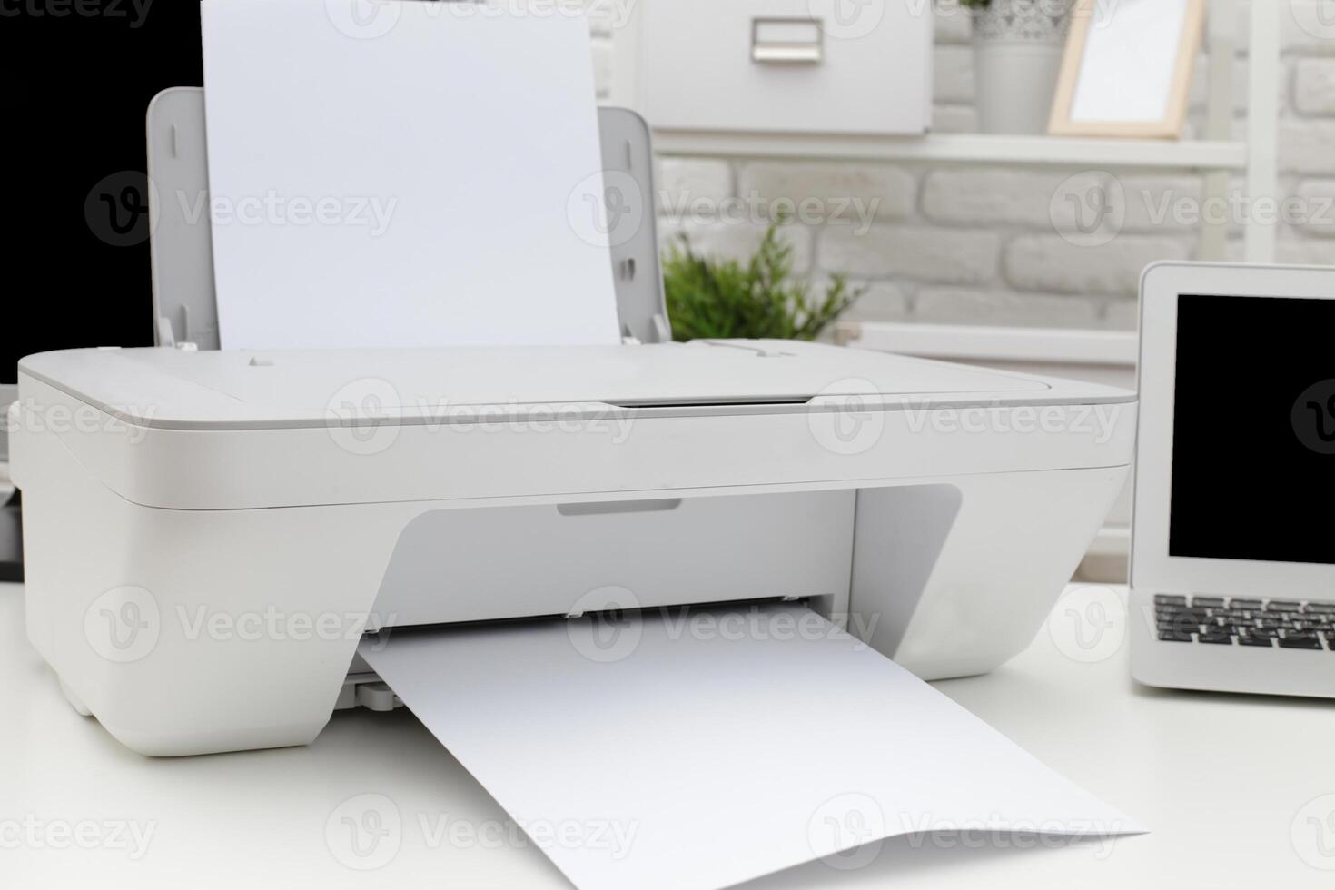 Modern printer printing documents on a white table in a cozy workspace with a laptop and decor photo