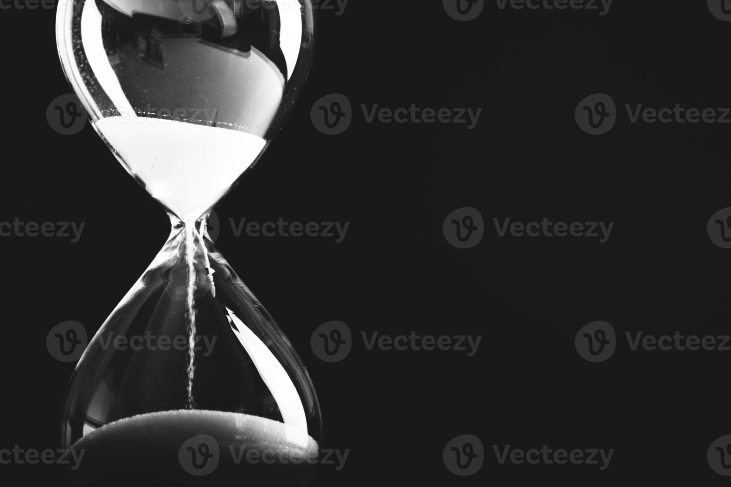 Sand flows in a glass hourglass creating a contrast against a dark background during a moment of reflection photo