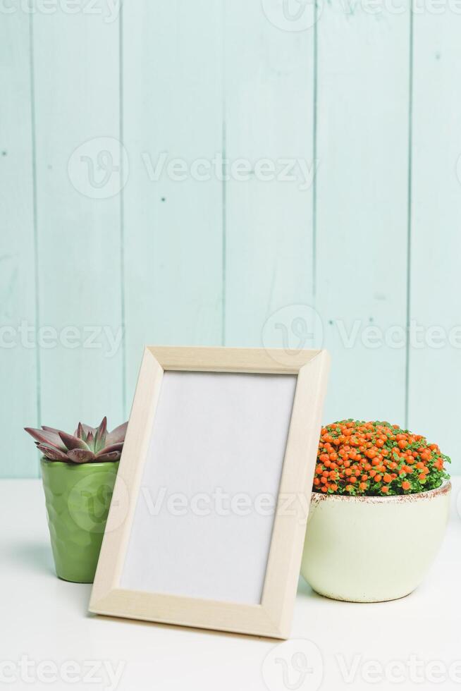 Decorative plant arrangements with a blank frame on a light blue wooden background in a cozy indoor setting photo