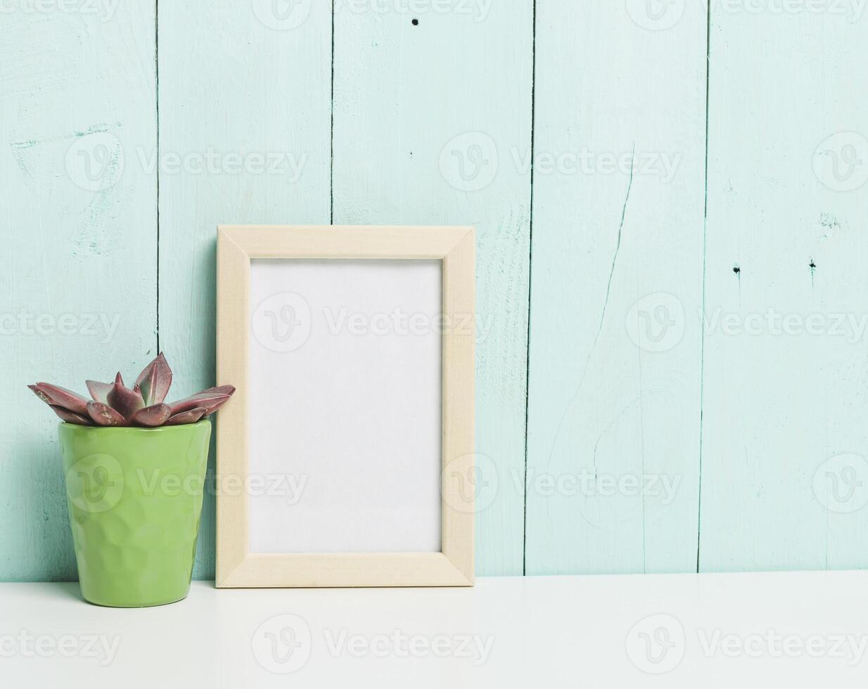 Simple and modern decor featuring a green plant and an empty frame against a light blue wooden wall photo