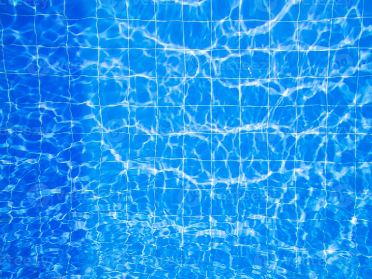 Clear blue water with sunlight reflections creating patterns in a swimming pool during a sunny day photo