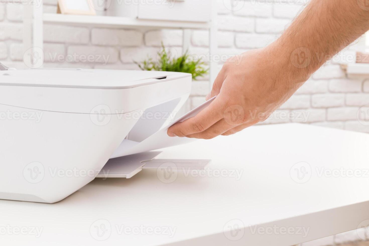Hand retrieving printed document from a white printer in a modern workspace photo