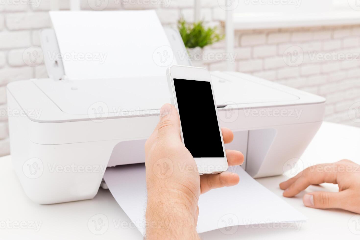 Person using smartphone to print document from home printer in bright workspace during the day photo