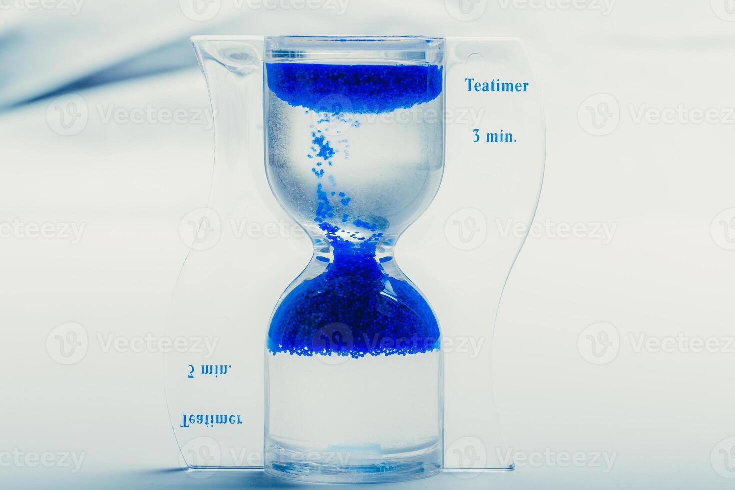 Unique hourglass timer with blue sand indicating three minutes for brewing tea photo