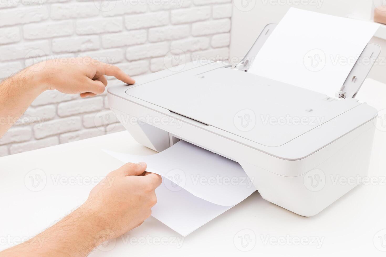 Person using a printer to retrieve a freshly printed document in a bright workspace with a brick background photo