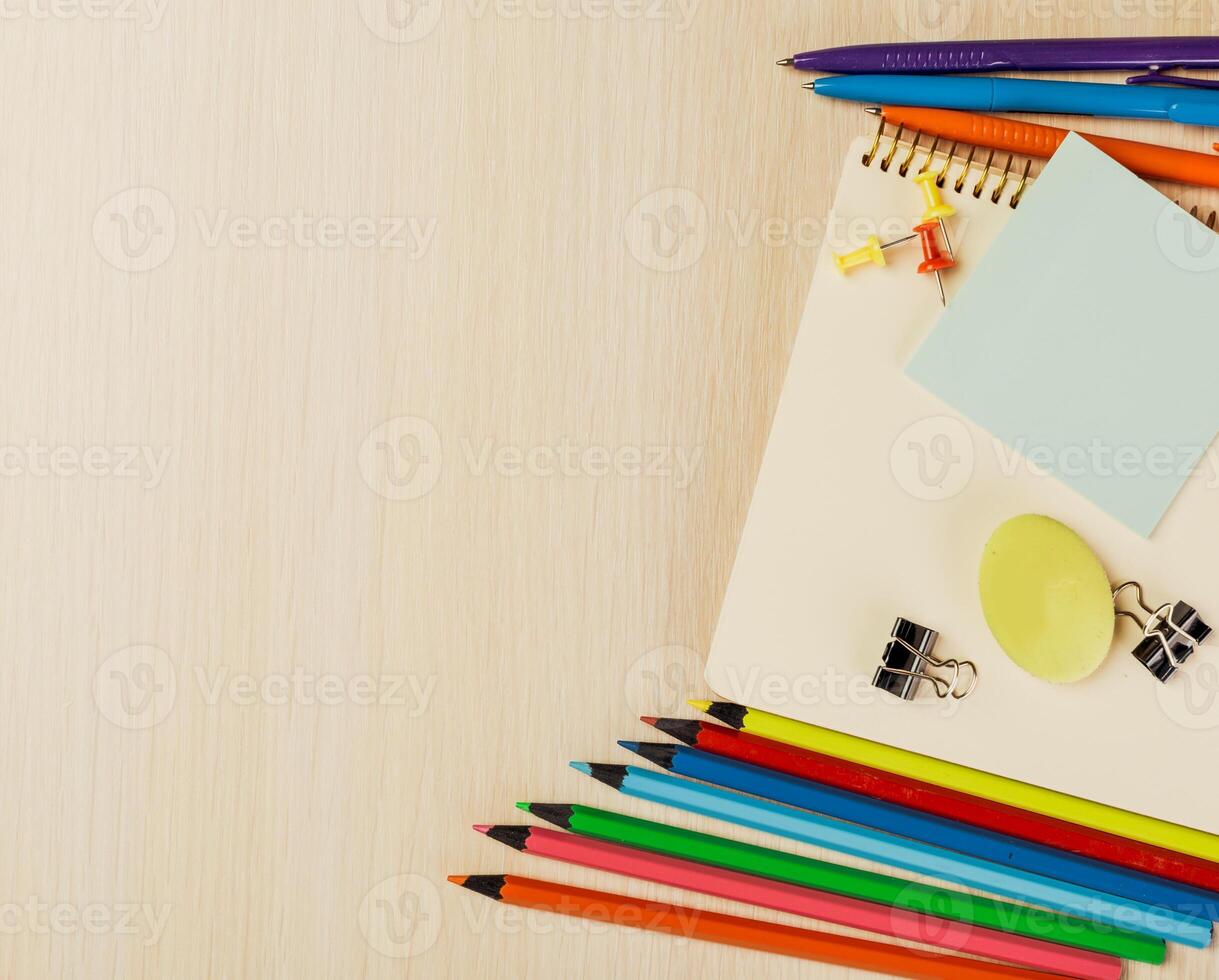 Colorful stationery arranged on a wooden table with notepad, paper clips, and markers in a bright workspace photo