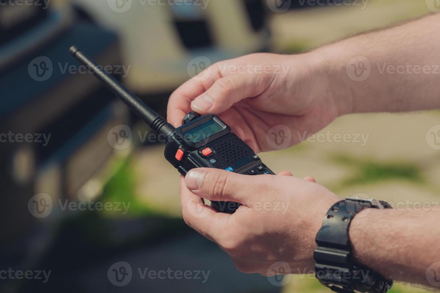 Hands holding a walkie-talkie in a rural outdoor setting during a sunny day photo