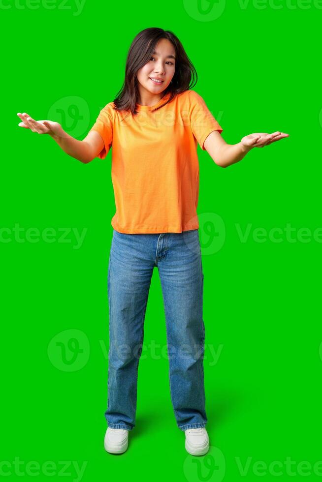 Young woman gesturing with hands in bright orange shirt and blue jeans on green background photo