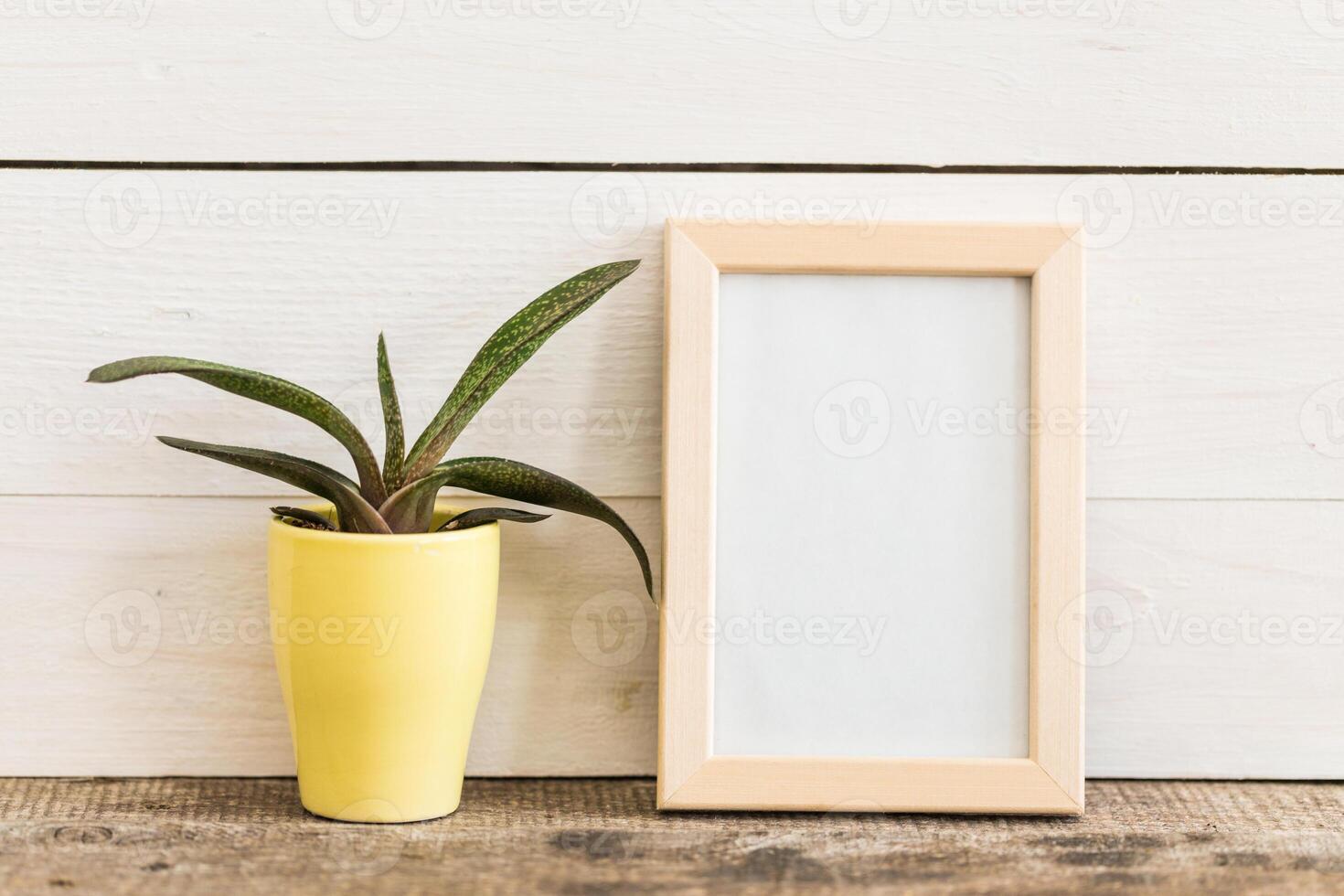 Simple home decoration with a yellow pot and empty picture frame on a wooden surface photo