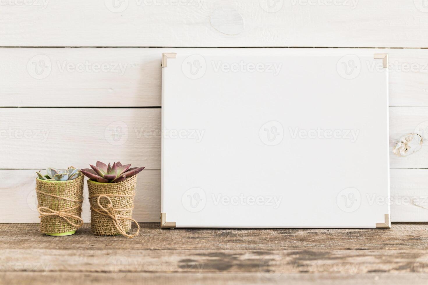 Decorative succulent pots next to an empty white board on rustic wooden table photo