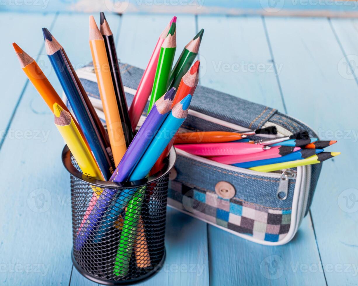 Colorful pencils in a black holder next to a pencil case on a blue wooden surface photo