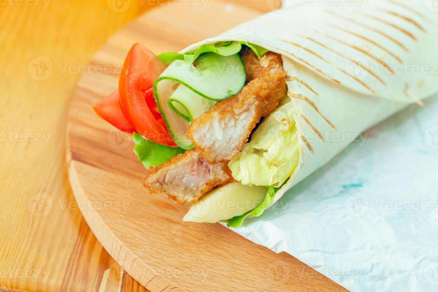 Delicious wrap filled with crispy chicken and fresh vegetables served on a wooden board photo