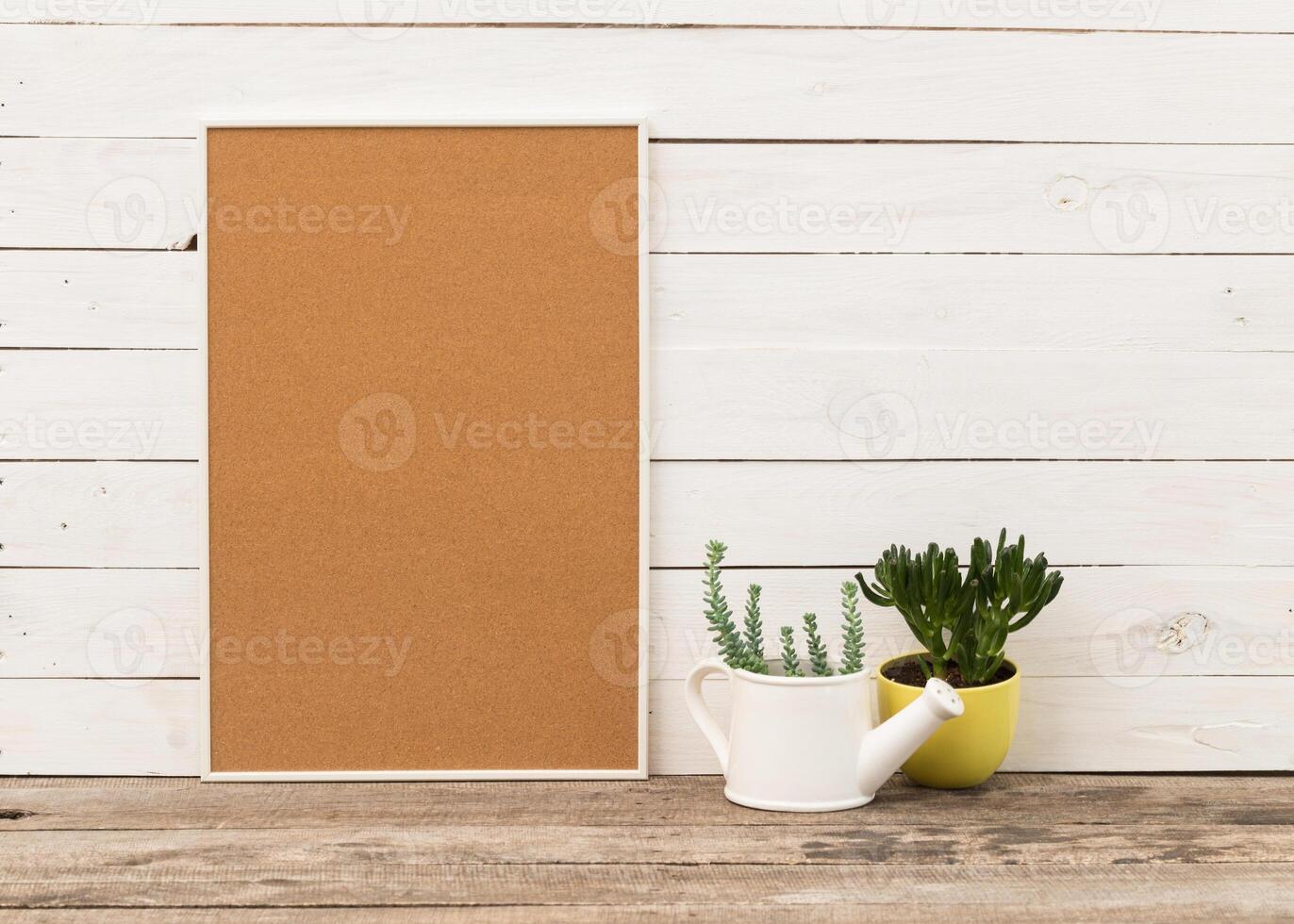 Simple decor setup with cork board, white planter, and succulent on wooden table against white wooden wall photo