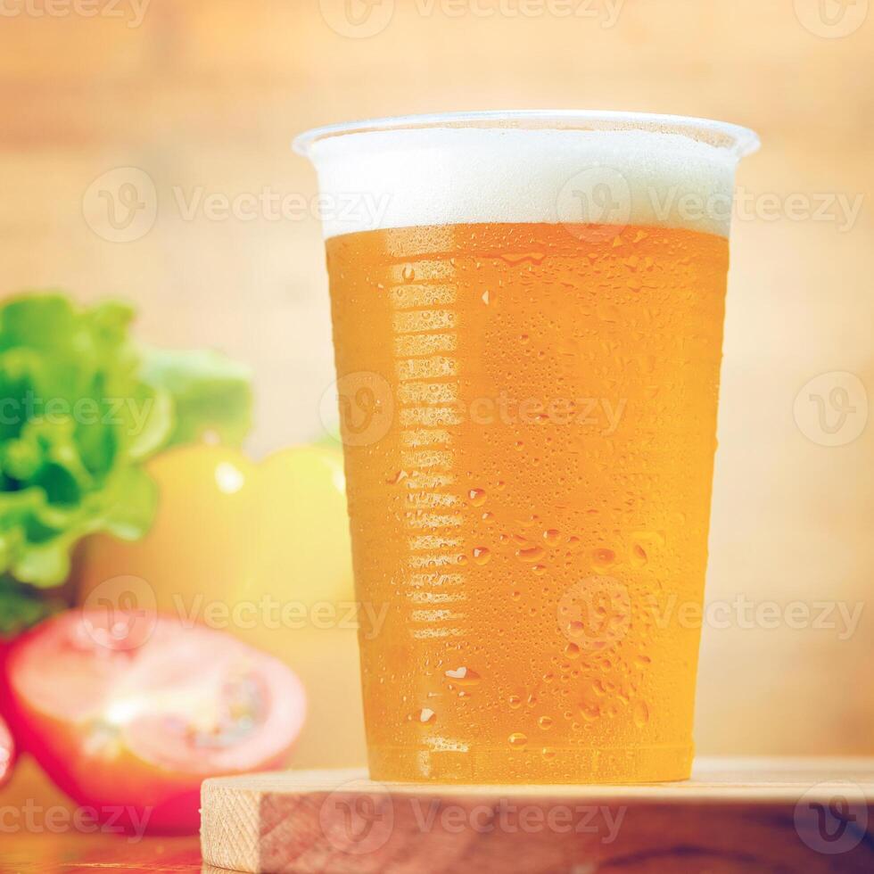 Refreshing craft beer served in a clear cup with chilled condensation against a backdrop of fresh vegetables and lemon photo