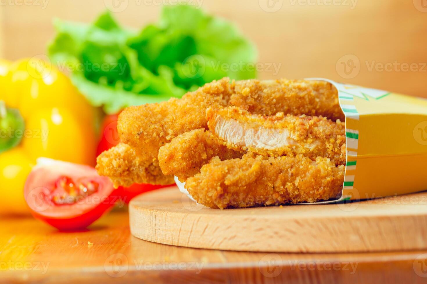 Crispy fried chicken tenders served with fresh vegetables on a wooden board photo