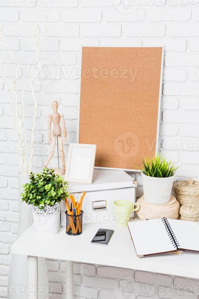 Creative workspace with plants and stationery organized on a white desk against a textured wall in a bright room photo