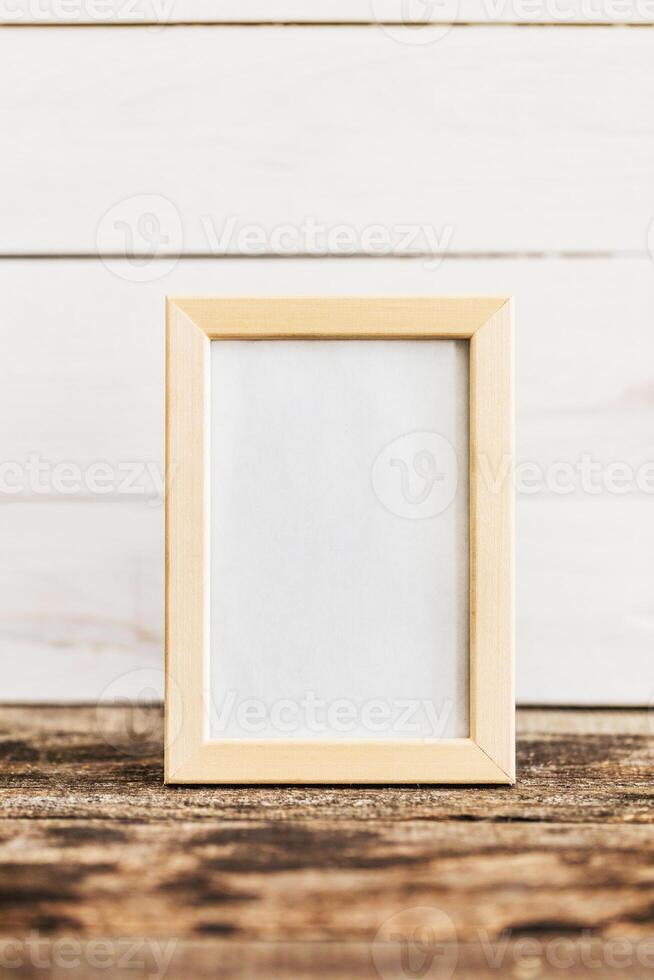 Empty picture frame displayed on a rustic wooden surface against a white wooden background photo
