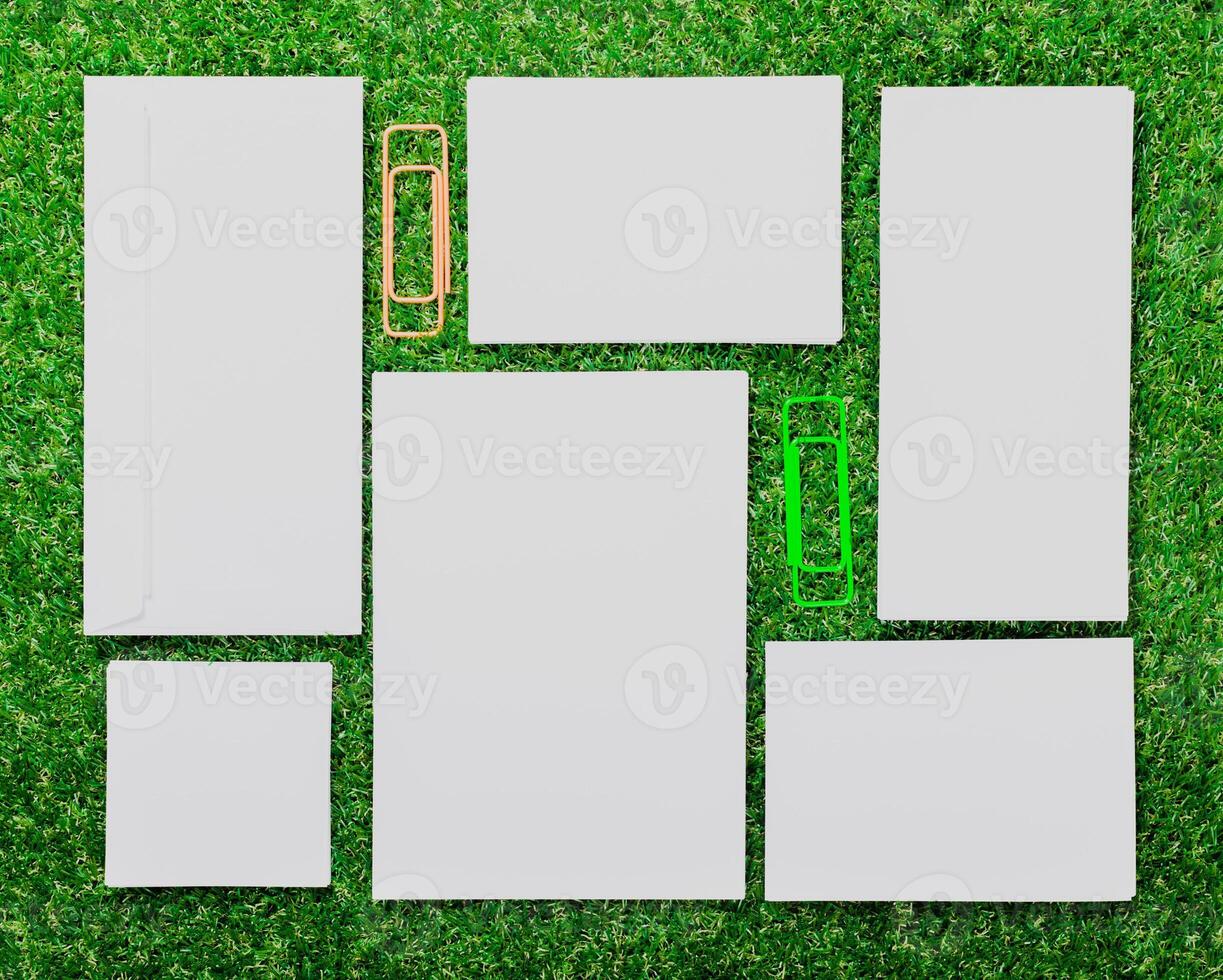 Blank paper sheets and paper clips arranged on green grass in a creative setup during daytime photo