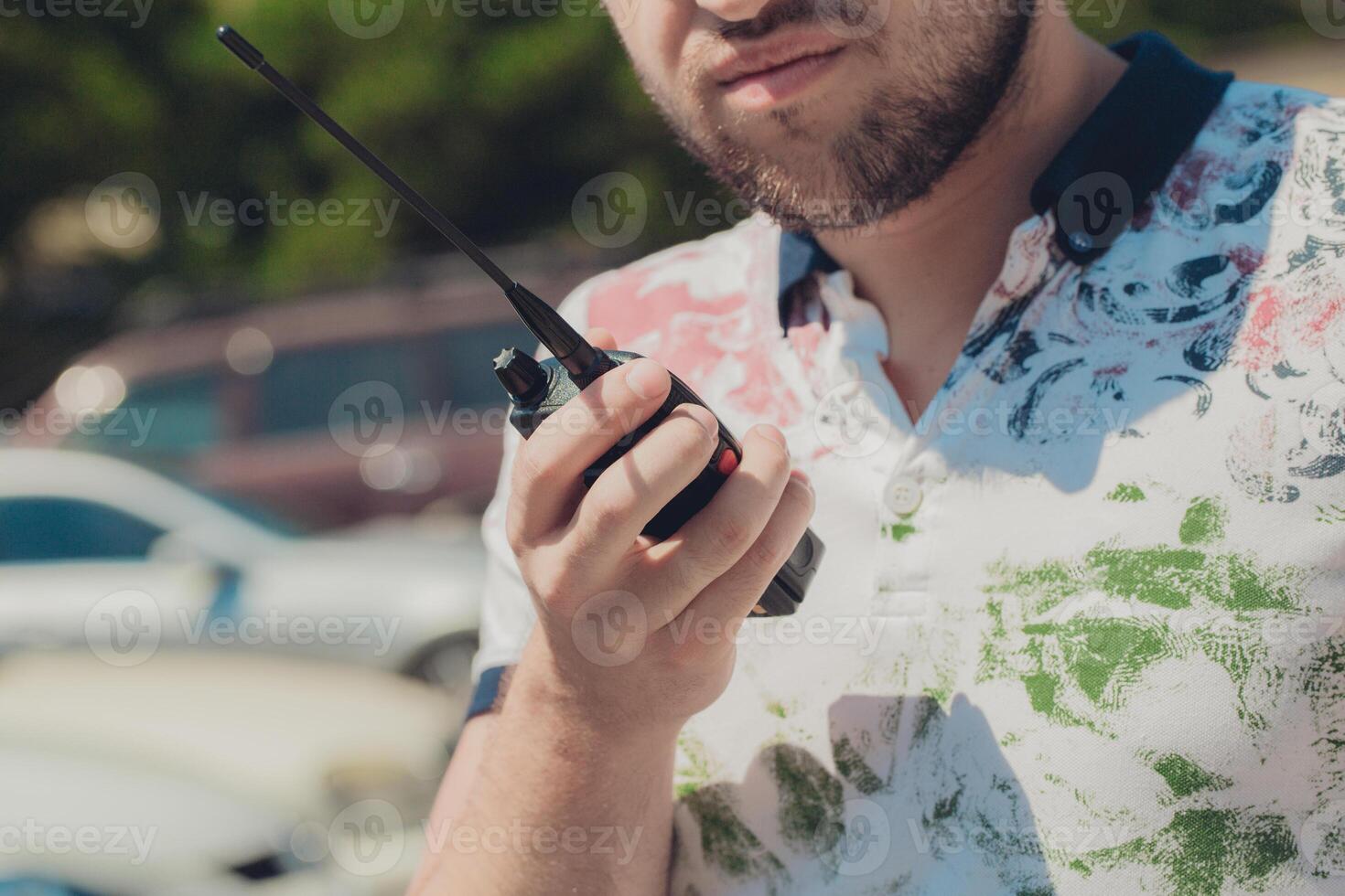 Man using a walkie-talkie wearing a colorful shirt in a parking lot during a sunny day photo