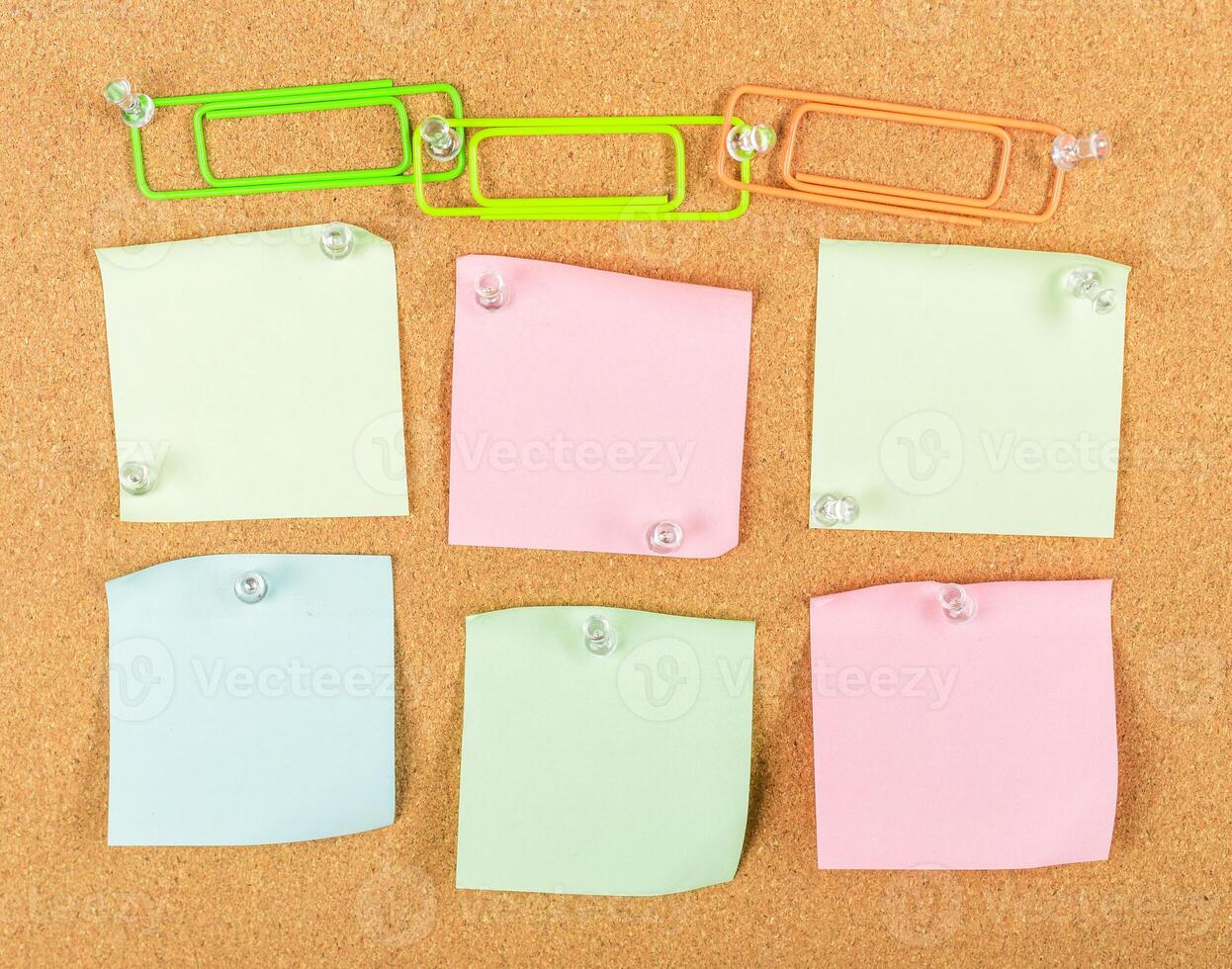 Colorful sticky notes and paper clips arranged on a corkboard for organizing ideas and reminders in an office setting photo