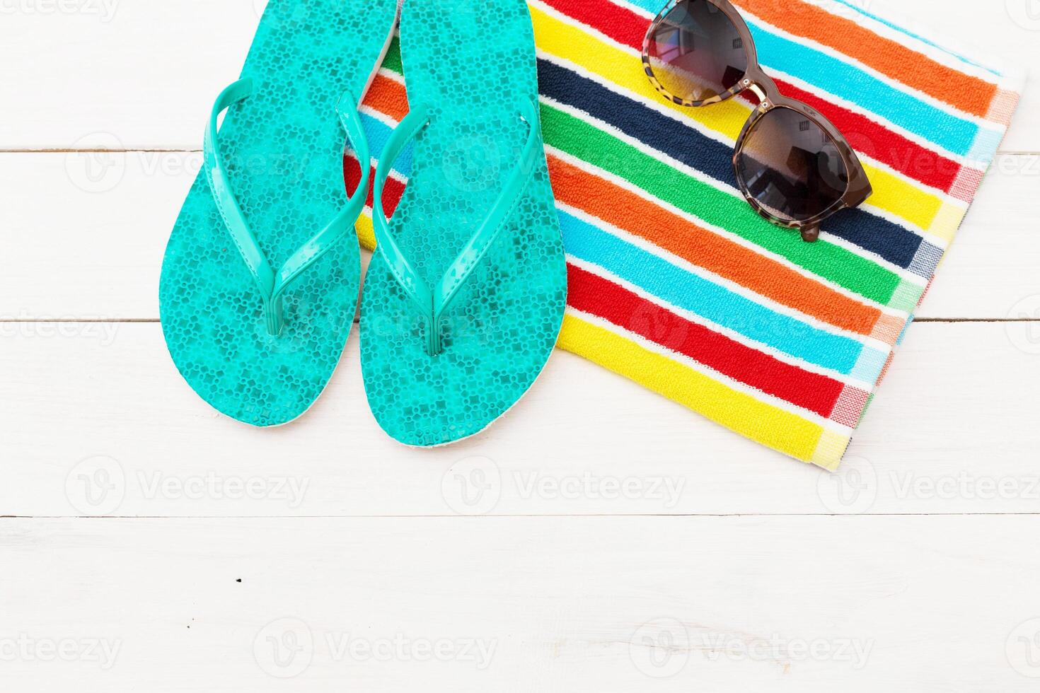 Summer essentials on a beach towel featuring colorful stripes with vibrant flip flops and stylish sunglasses photo