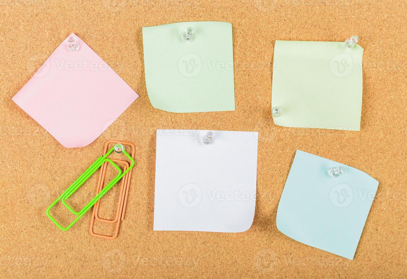 Colorful sticky notes and paper clips arranged on a cork board with push pins during a daylight workspace setup photo