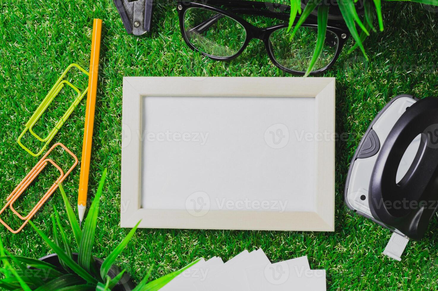 Workspace setup with blank picture frame, stationery, and greenery during daylight hours photo
