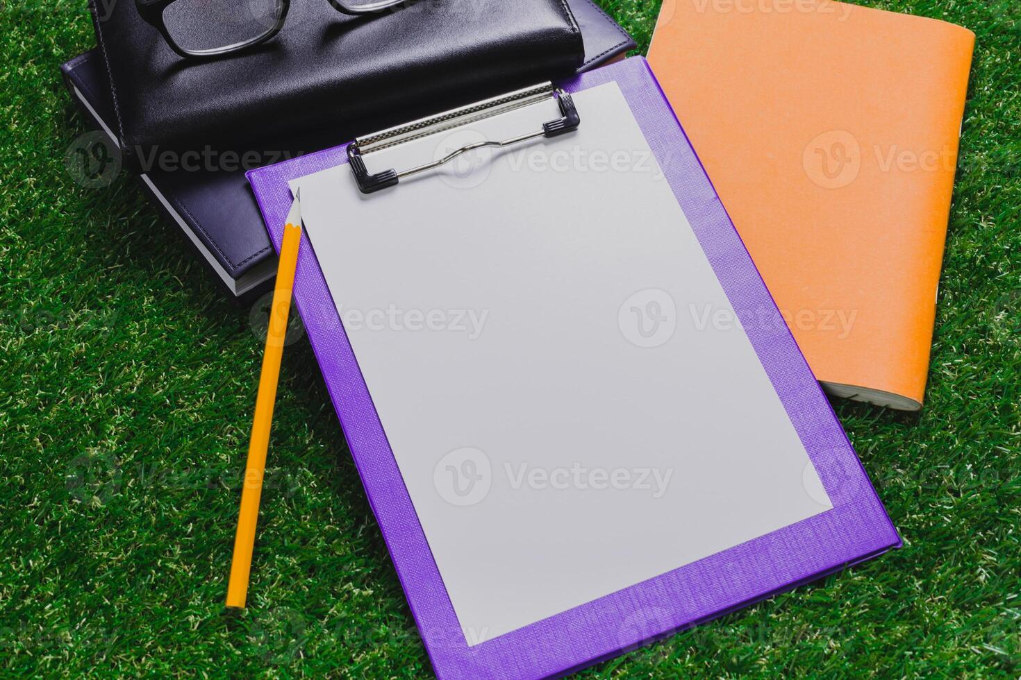 Blank notepad and clipboard ready for notes on green grass during sunny day in the park with notebooks nearby photo