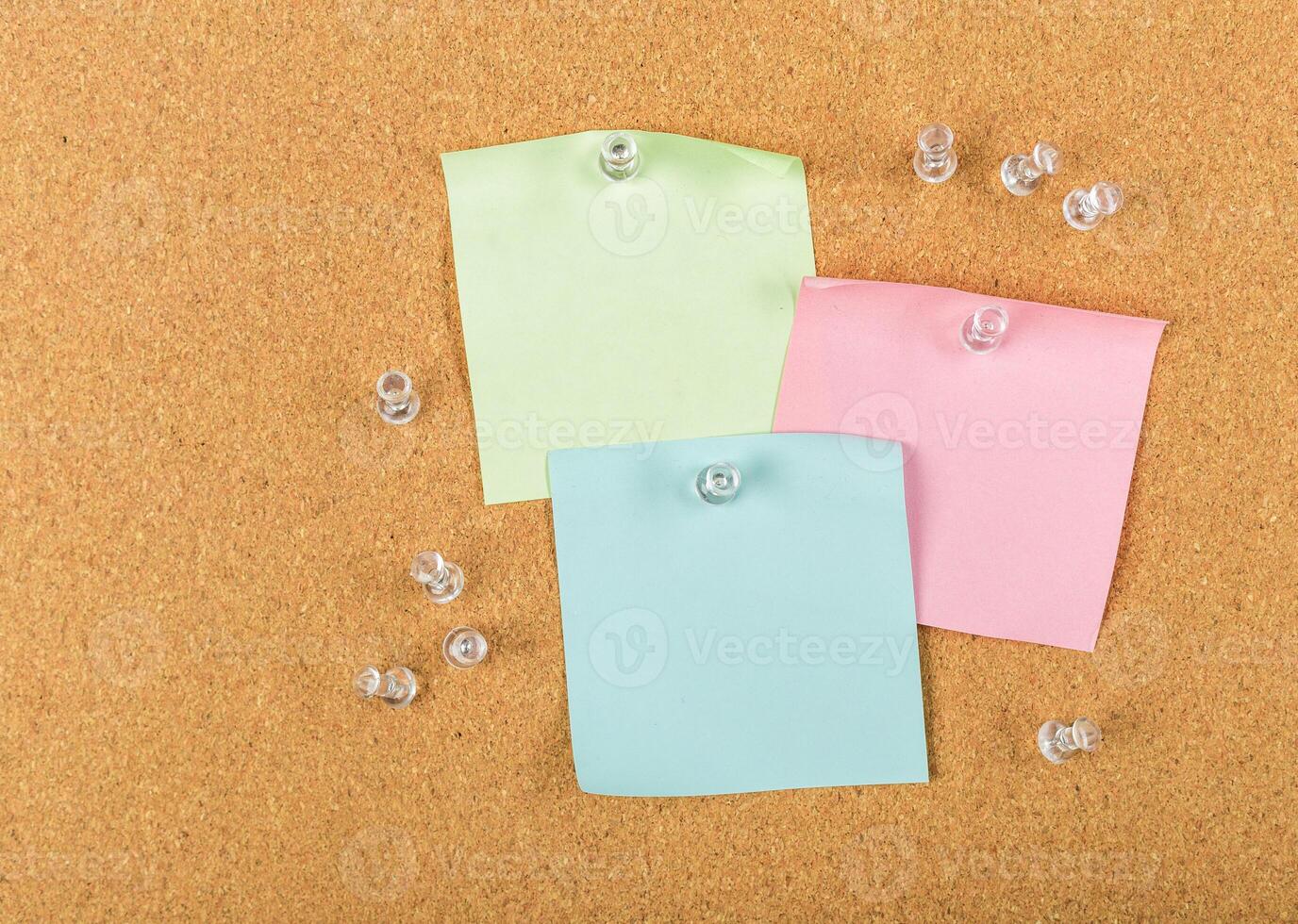 Colorful sticky notes pinned on corkboard surface with clear push pins scattered around photo