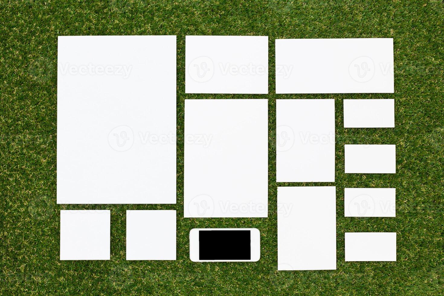 White paper sheets arranged neatly on a green grass surface with a smartphone placed among them for creative design purposes photo