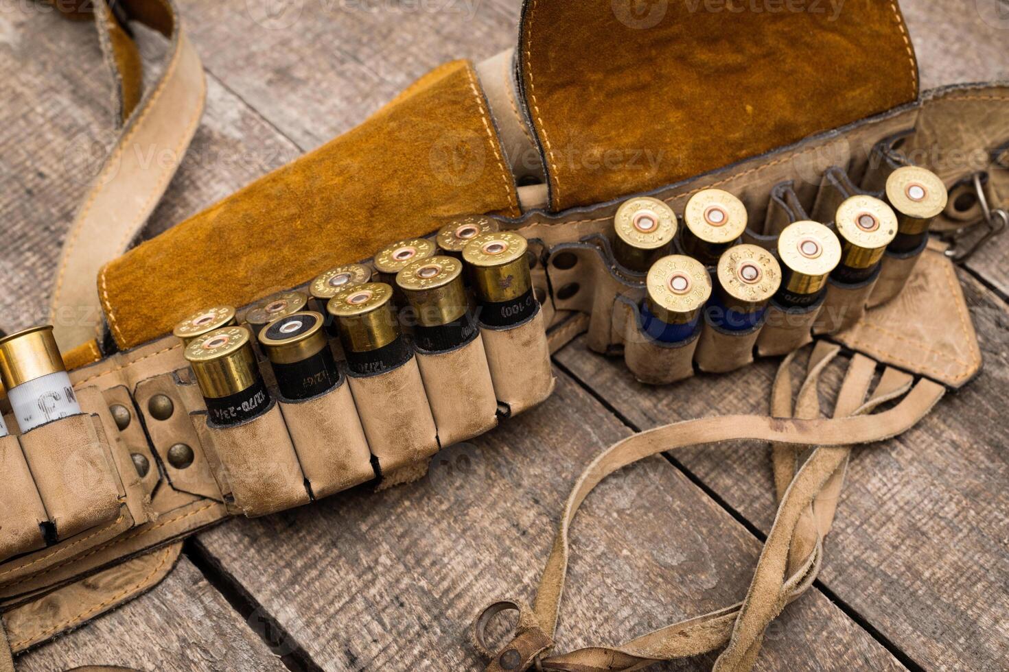 Leather ammunition belt displaying various shotgun shells resting on a rustic wooden surface photo