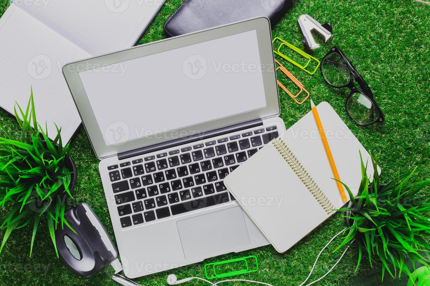 Workspace setup on green grass featuring a laptop, notebook, and various office supplies during a sunny day photo