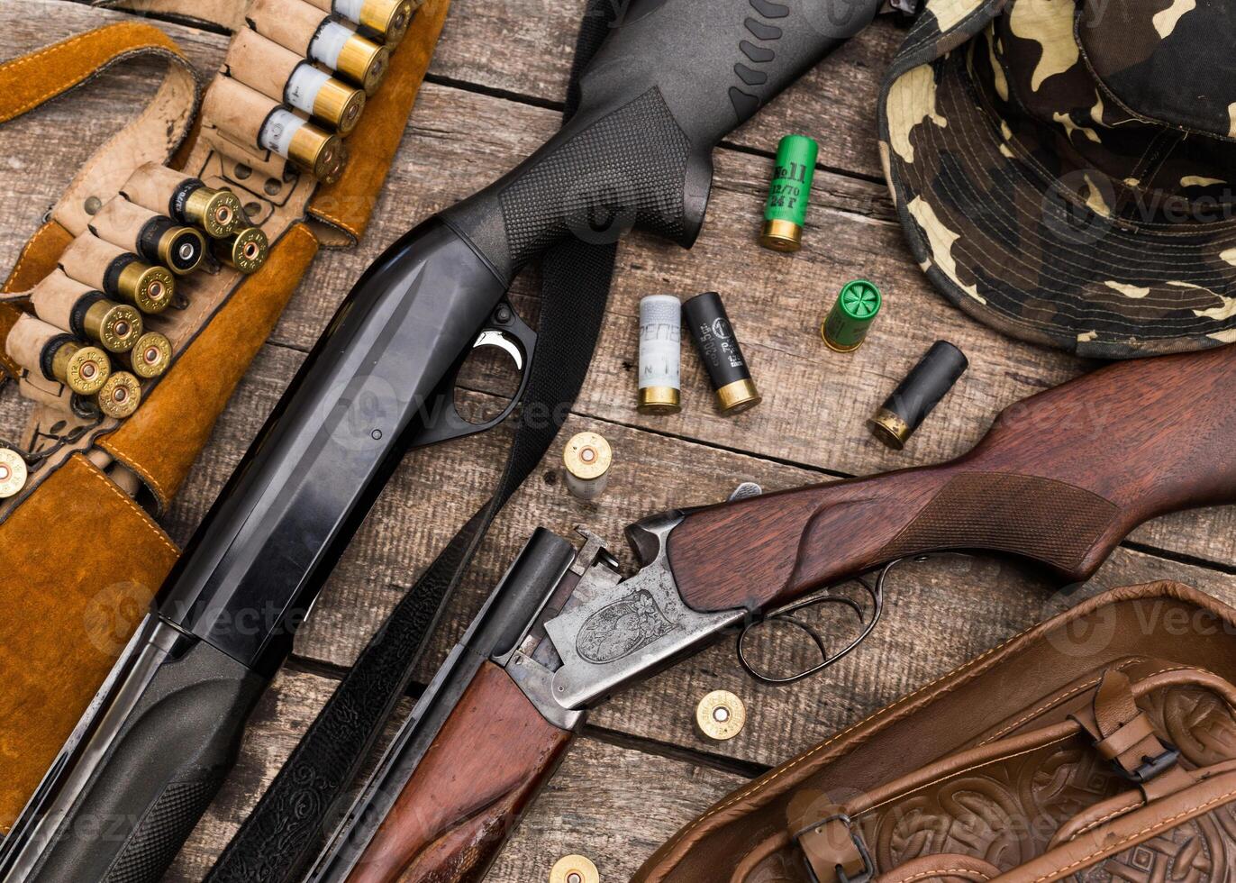 Guns and hunting gear displayed on wooden table with ammunition and camouflage hat photo