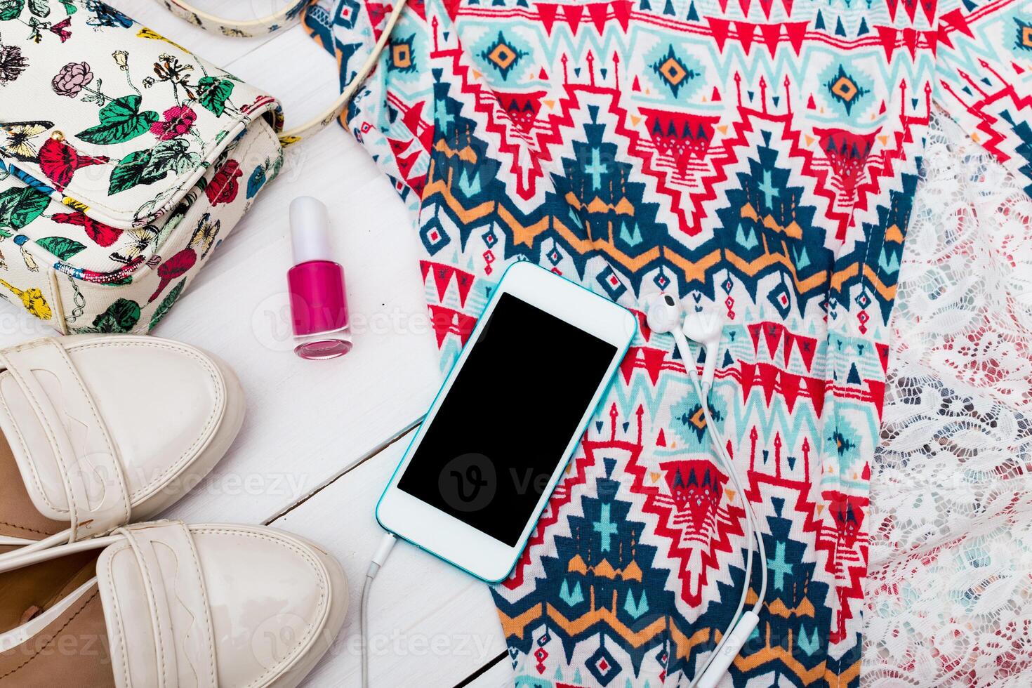 Brightly patterned summer outfit laid out with accessories and a smartphone on a light wooden surface photo