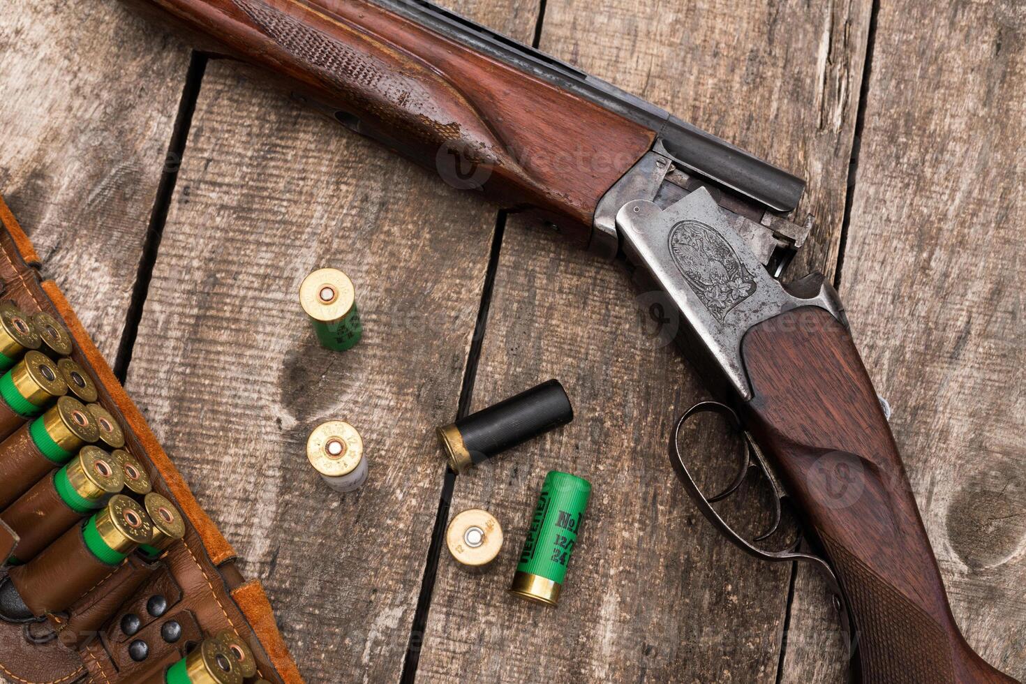 Vintage shotgun resting on a wooden table with scattered ammunition and a leather shell holder nearby photo