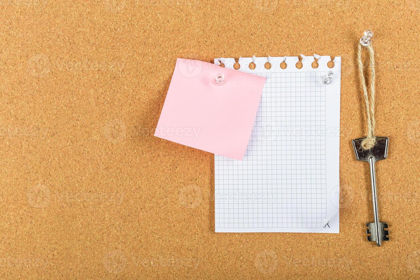 Note-taking setup with a blank grid sheet, a pink sticky note, and a vintage key on corkboard at home office workspace photo