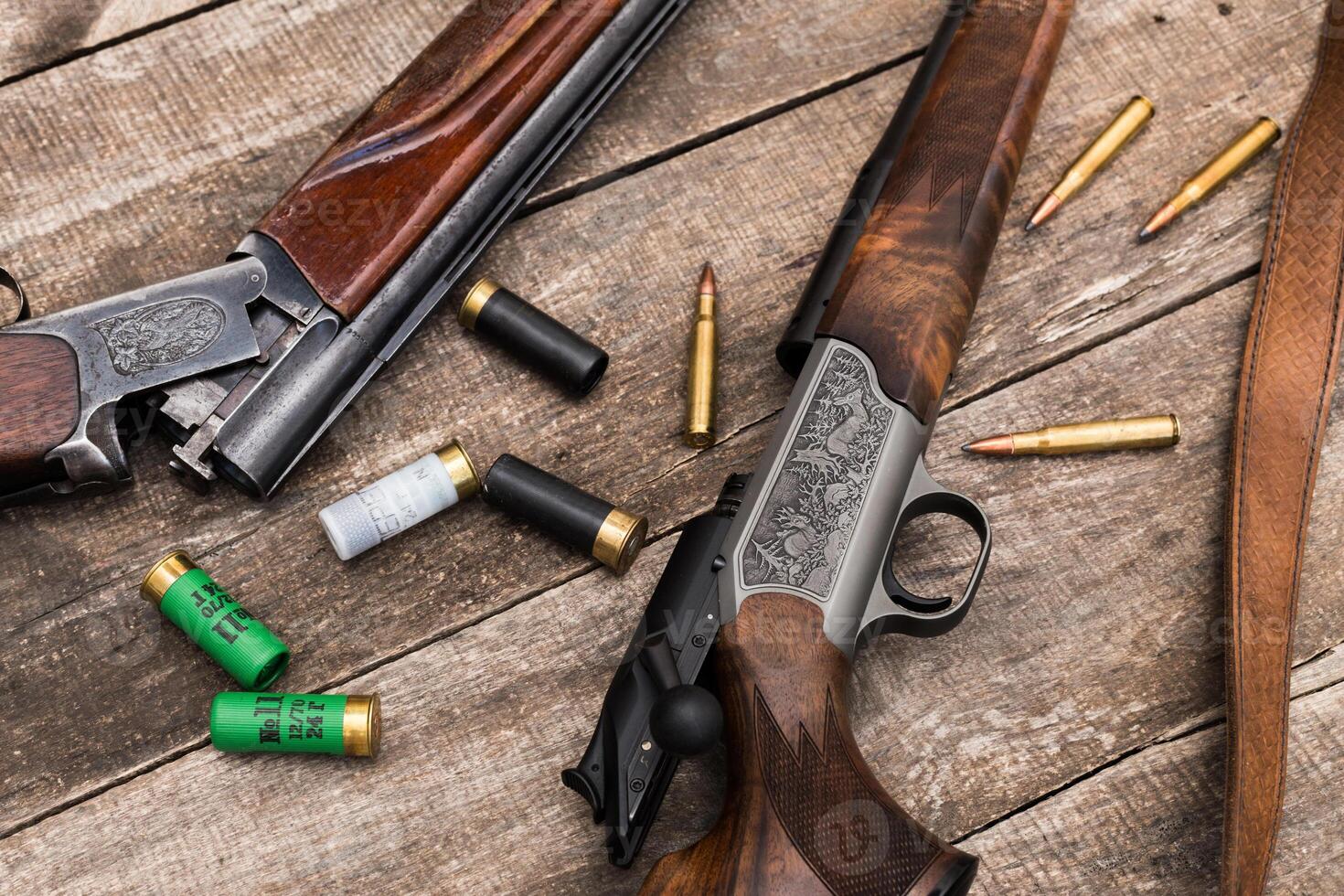 Vintage hunting equipment displayed on a wooden surface with ammunition and shotgun shells organized around the firearms photo