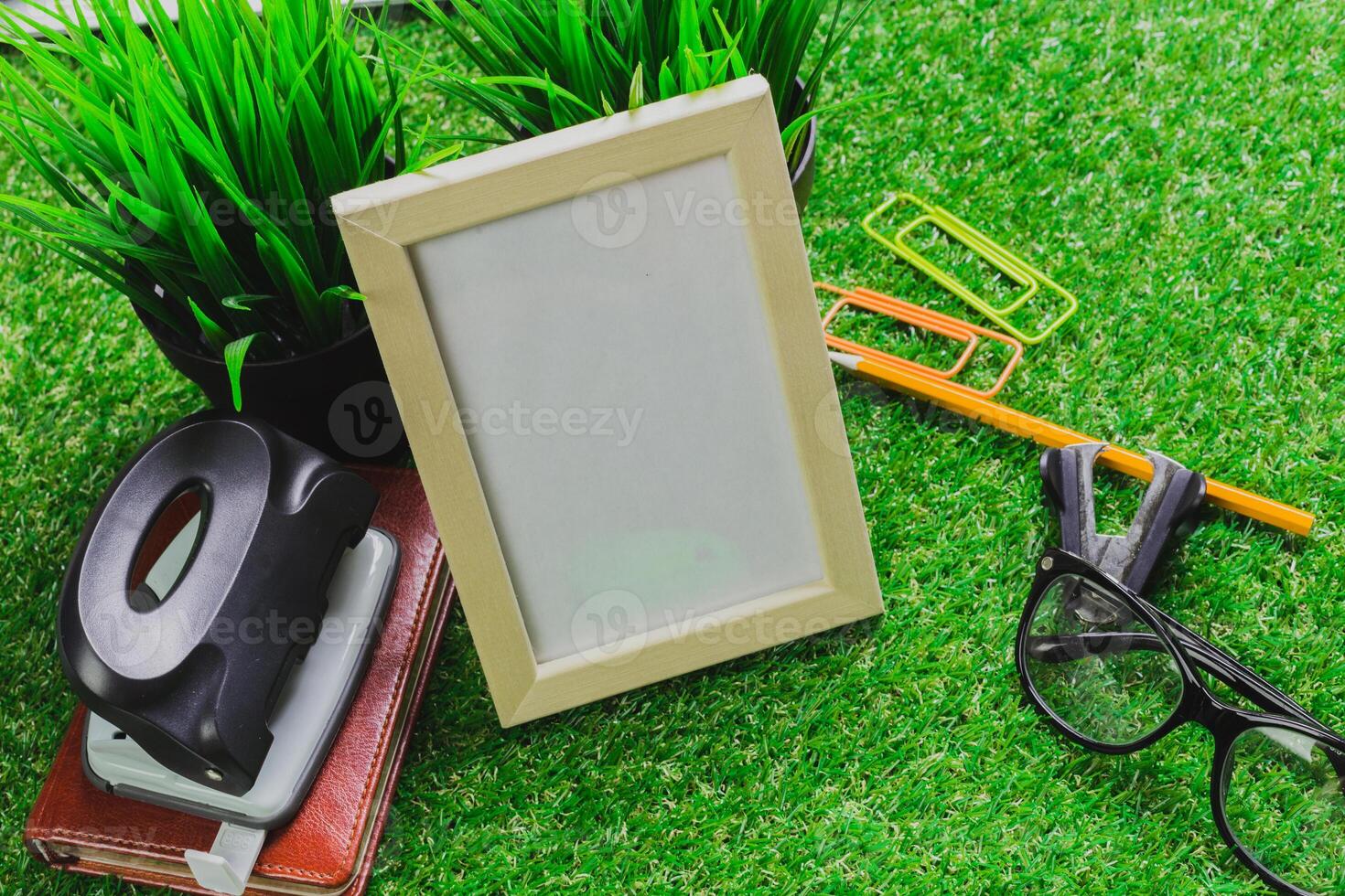 Workspace setup featuring a blank picture frame, stationery, and greenery on a tabletop in a bright environment photo
