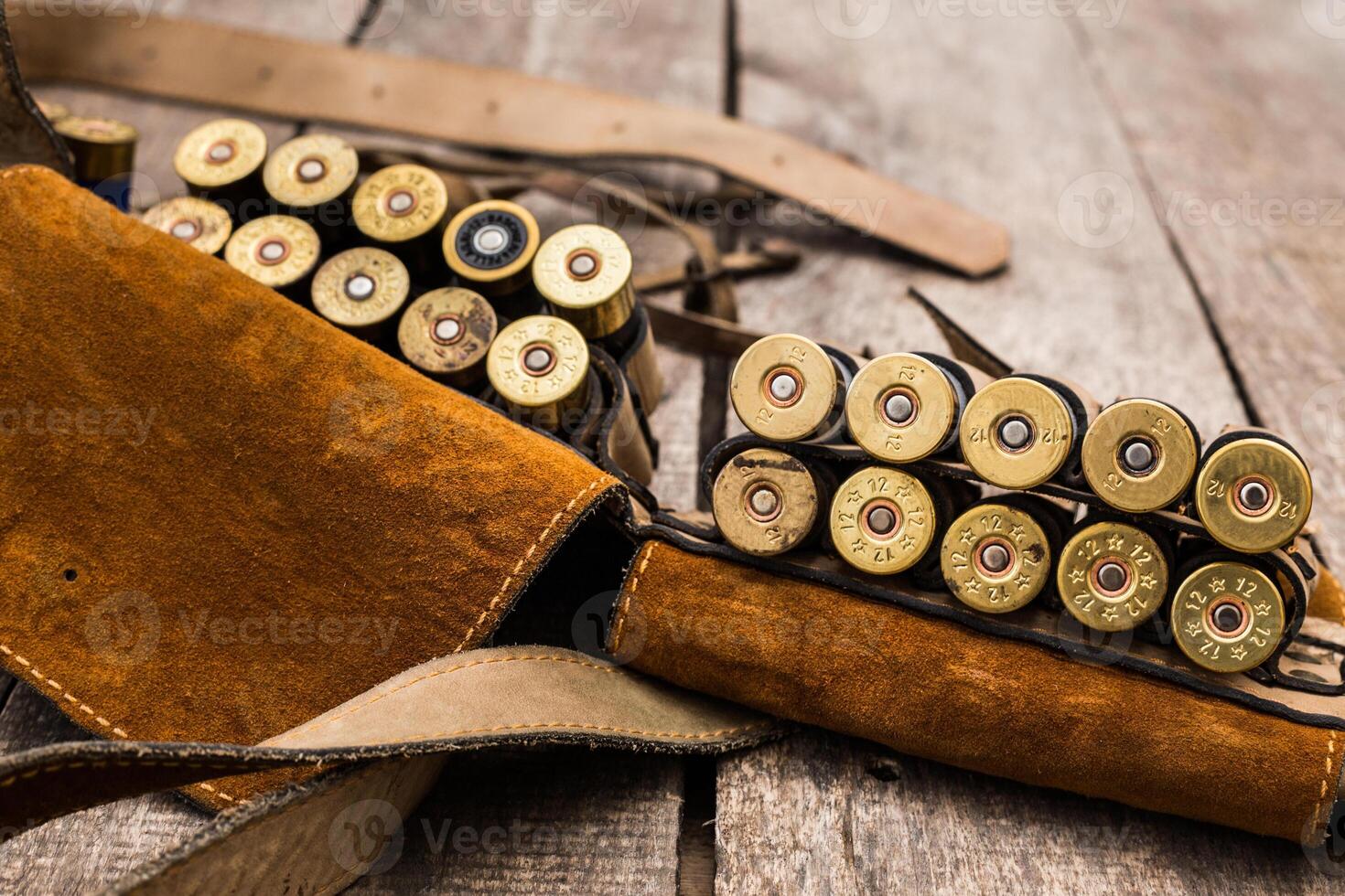 Shotgun shells and leather holder arranged on rustic wooden surface in hunting setup photo