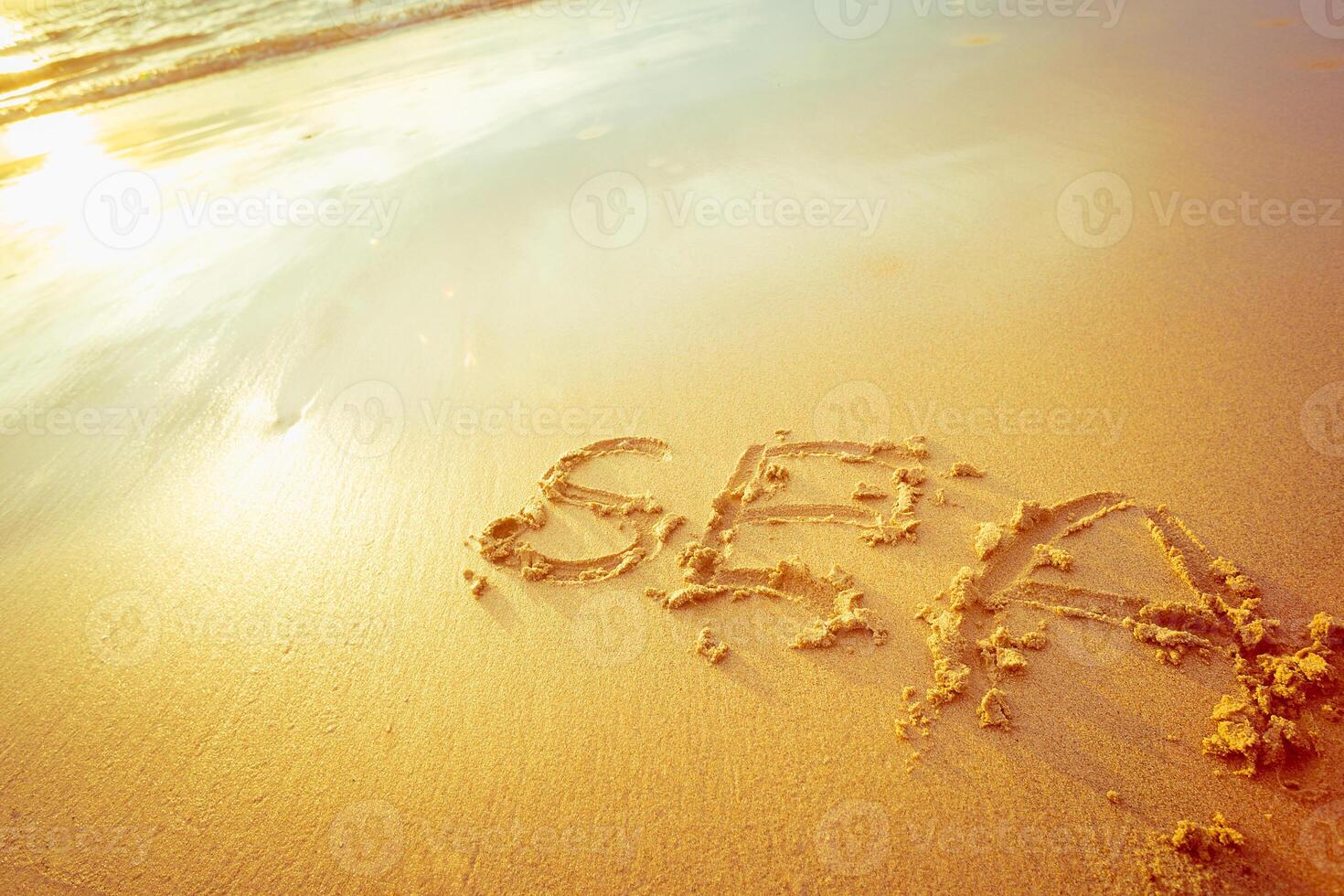 Waves gently wash over sandy beach where the word sea is written at sunset photo