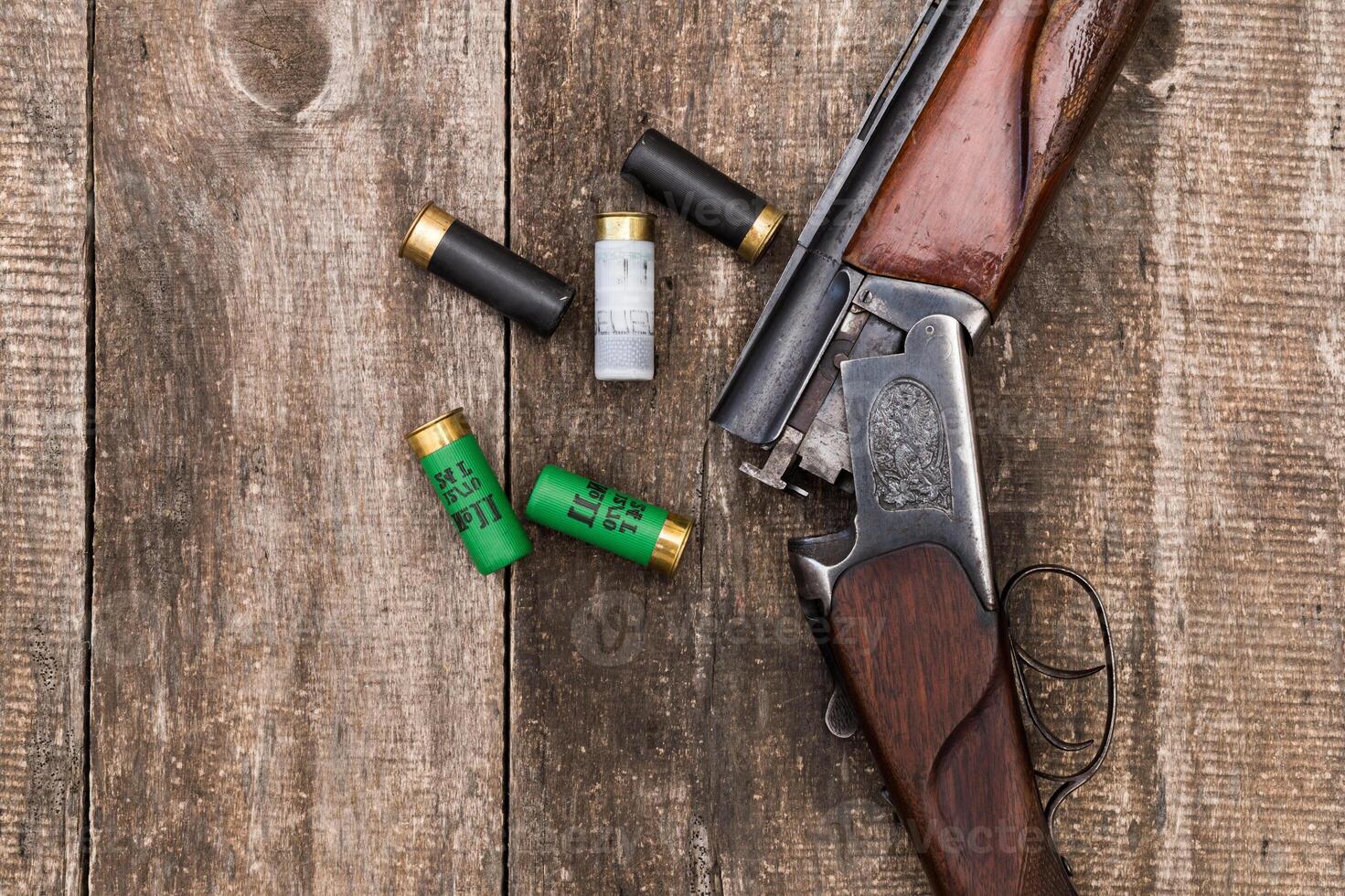 Vintage shotgun and ammunition resting on wood surface in a rustic setting during daylight hours photo