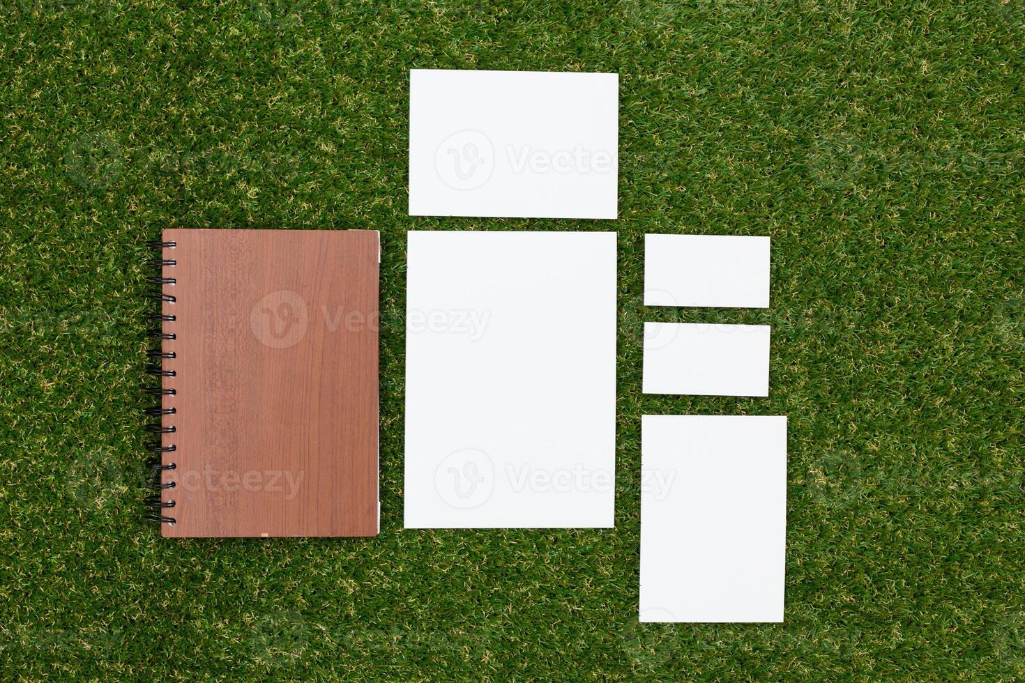 Collection of blank papers and a notebook arranged on green grass in bright sunlight photo