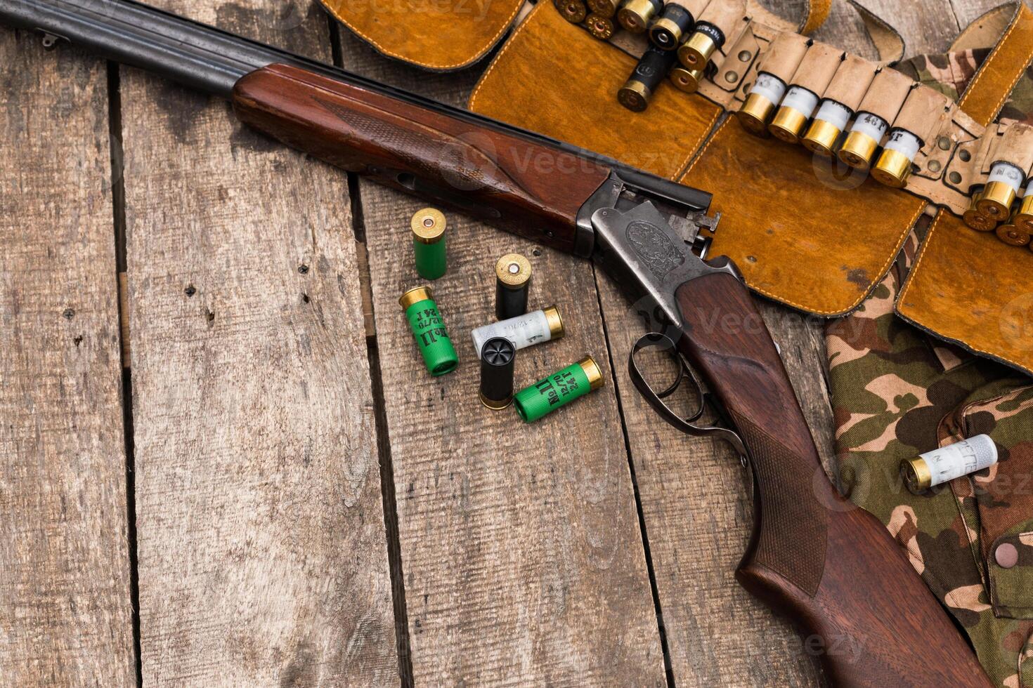 Classic shotgun and ammunition displayed on rustic wooden surface with camouflage cloth photo