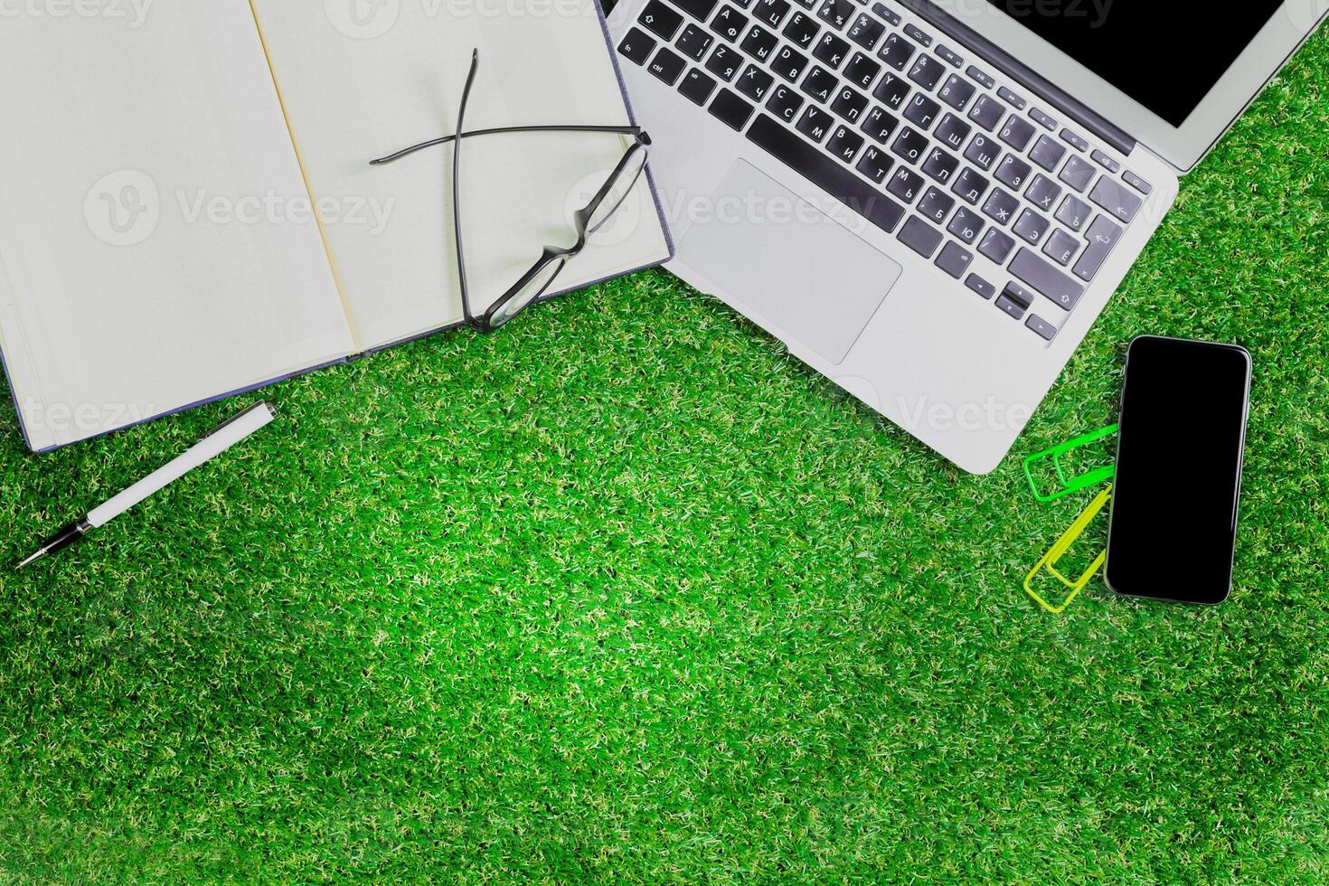 Workspace setup on artificial grass with laptop, notebook, and smartphone during a casual outdoor study session photo