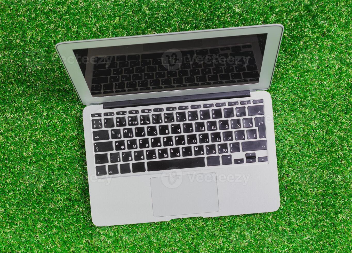 Laptop resting on green artificial grass with a reflective screen in an outdoor setting during daylight hours photo