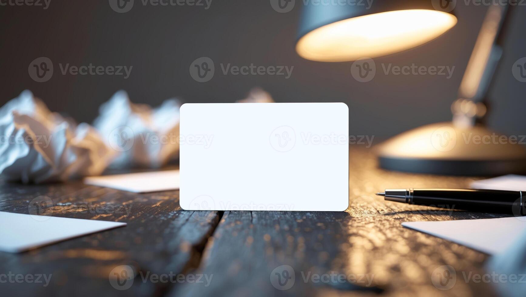 Workspace with blank card and pen on wooden table illuminated by desk lamp in a quiet setting photo
