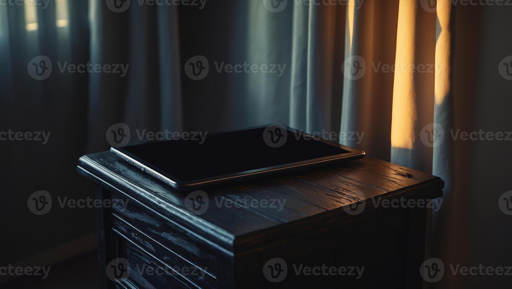 Tablet resting on a wooden table with sunlight streaming through curtains in a dimly lit room during late afternoon photo