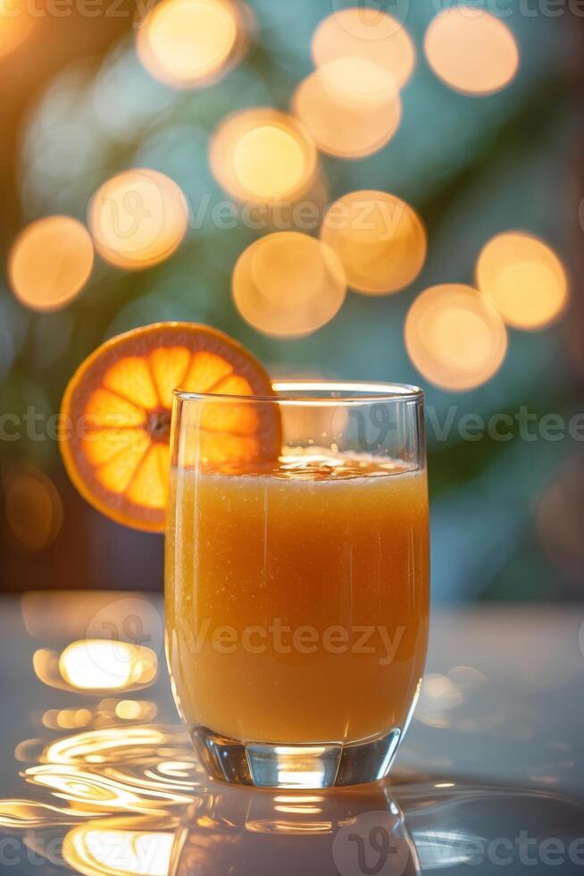 Refreshing orange drink served in a clear glass on a reflective surface with glowing bokeh background photo