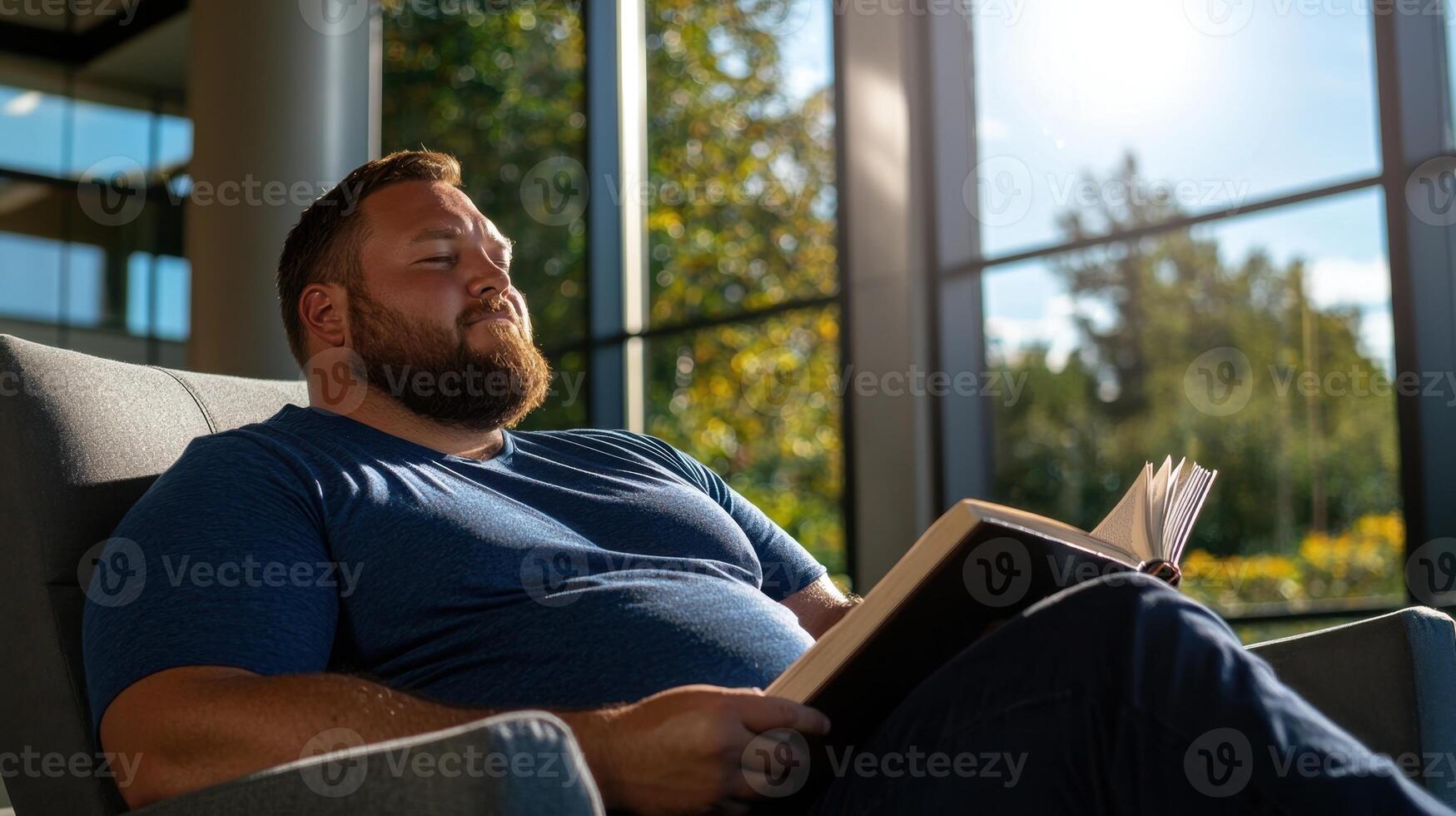 A man with a beard sitting in a chair reading a book photo