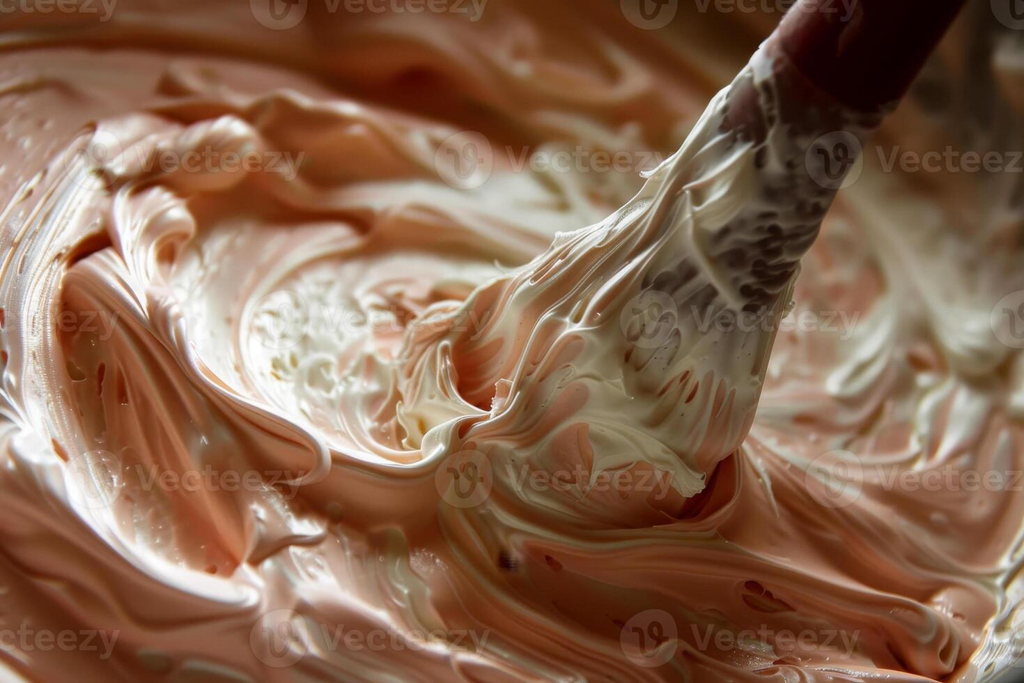 A spoon is used to mix a creamy white and pink frosting photo
